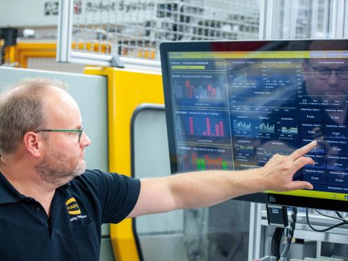 Person bedient Touch-Monitor mit Produktionskennzahlen in Industrieumgebung