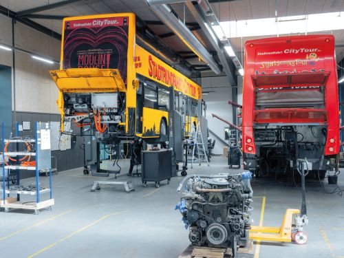Montagehalle mit zwei Bussen mit geöffneter Heckklappe, der Dieselmotor ist bereits ausgebaut