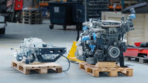 Dieselmotor im ausgebauten Zustand auf einer Palkette neben dem etwa halb so großen Elektromotor
