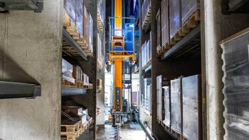 High-bay warehouse with pallets, a storage and retrieval machine moves between them.