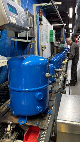 Mitarbeiter an einer Produktionslinie mit mehreren blau lackierten Hubkolbenverdichtern.