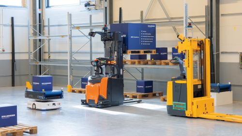 Three driverless transport systems of different designs are manoeuvring in a high-bay warehouse.