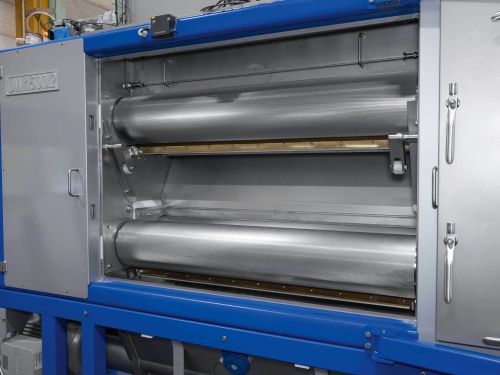 Two stainless steel rollers, one above the other, in a grinding mechanism