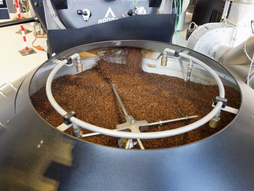 A stainless steel container with a stirring arm, filled with coffee beans.