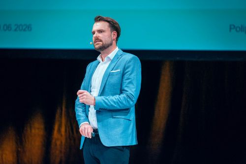 Frederik Meyer von POLIPOL hält einen Vortrag auf einer Bühne, trägt ein blaues Sakko und spricht mit einem Headset-Mikrofon.