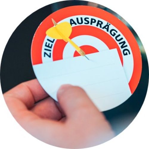 Foto: Eine runde Karte wird hochgehalten . Eine Zielscheibe ist abgebildet.