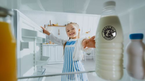 A girl looks into a fridge and reaches for a milk bottle.